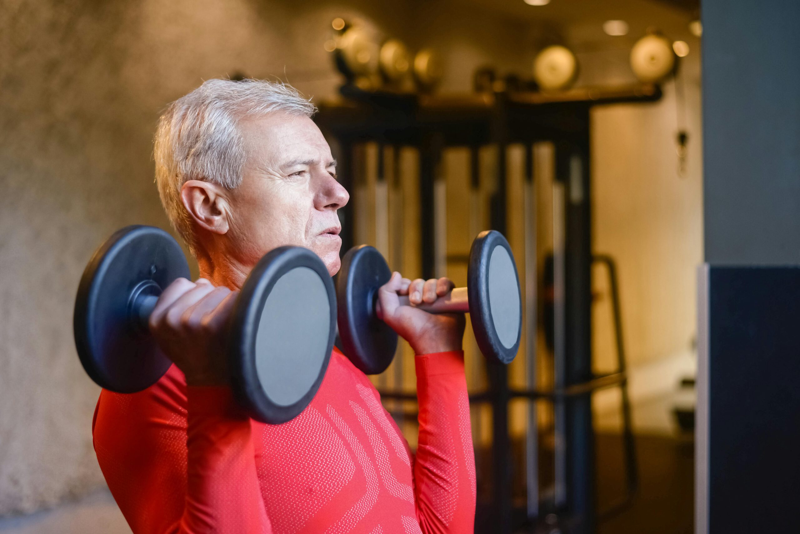 Elderly man lifting dumbbells at the gym to maintain a healthy lifestyle and stay fit.
