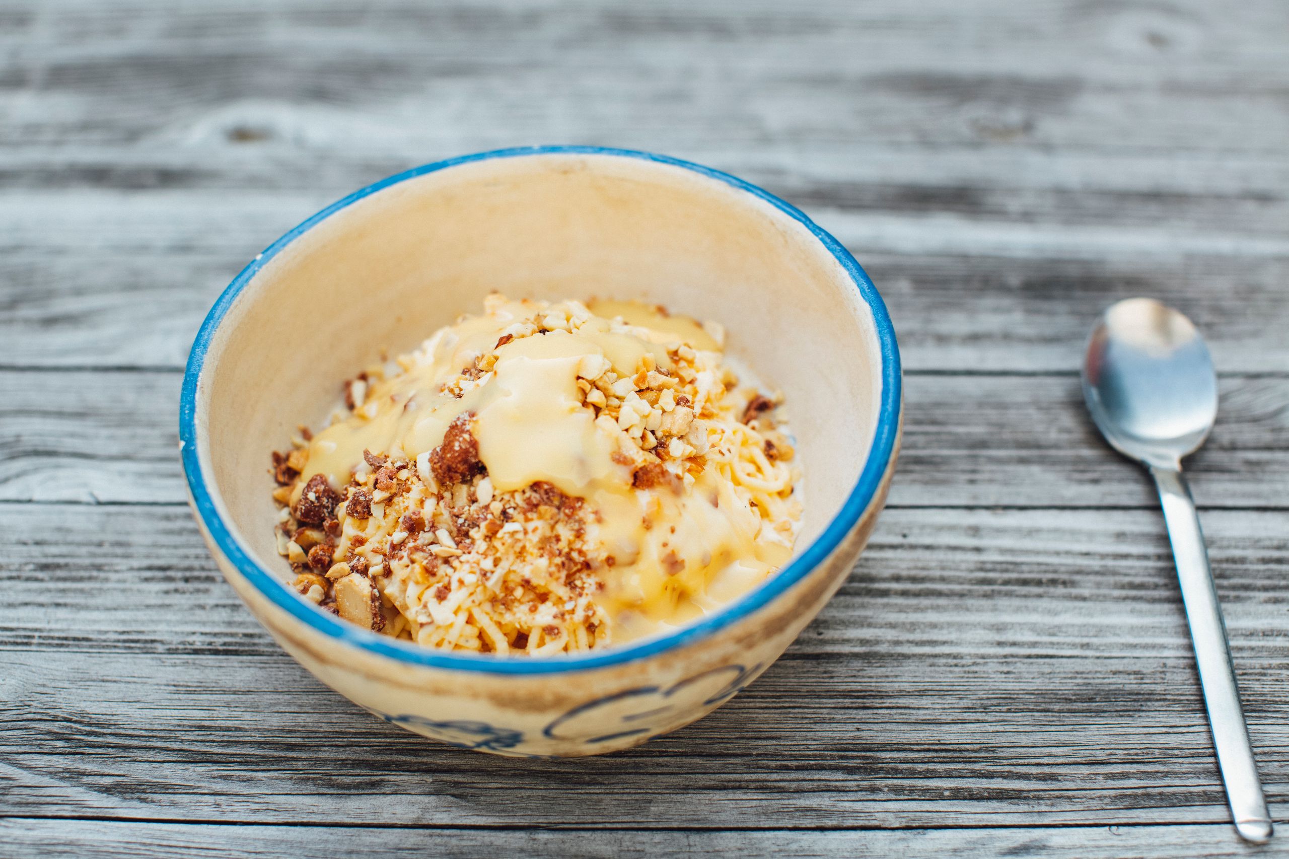 A close-up of a dessert bowl with creamy sauce and nuts on a rustic wooden table.