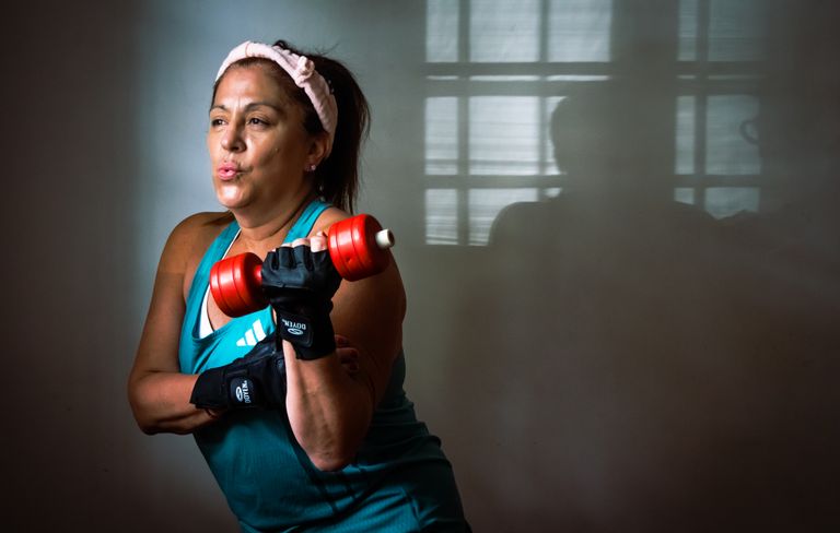 A middle-aged woman exercising indoors with a red dumbbell, showcasing strength and fitness motivation.