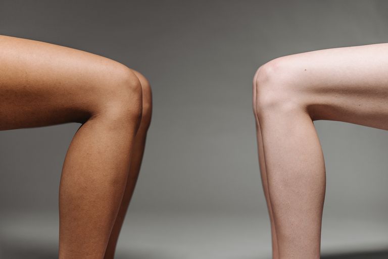 Close-up shot of two diverse human legs against a gray studio background.