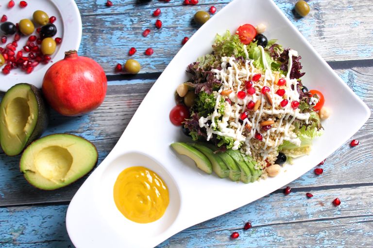 Colorful avocado quinoa salad with pomegranate and olives, on a rustic wooden table.