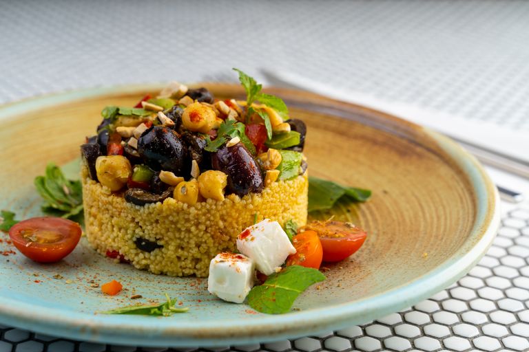 Delicious couscous salad with olives, chickpeas, and cherry tomatoes on a modern plate.
