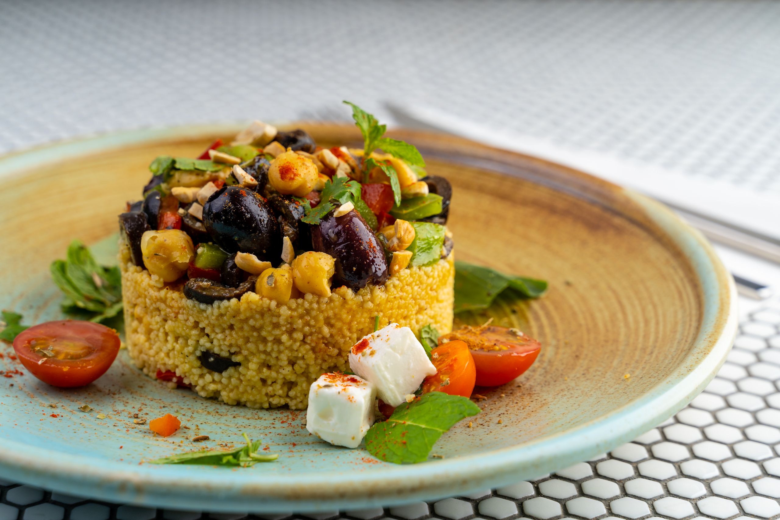 Delicious couscous salad with olives, chickpeas, and cherry tomatoes on a modern plate.
