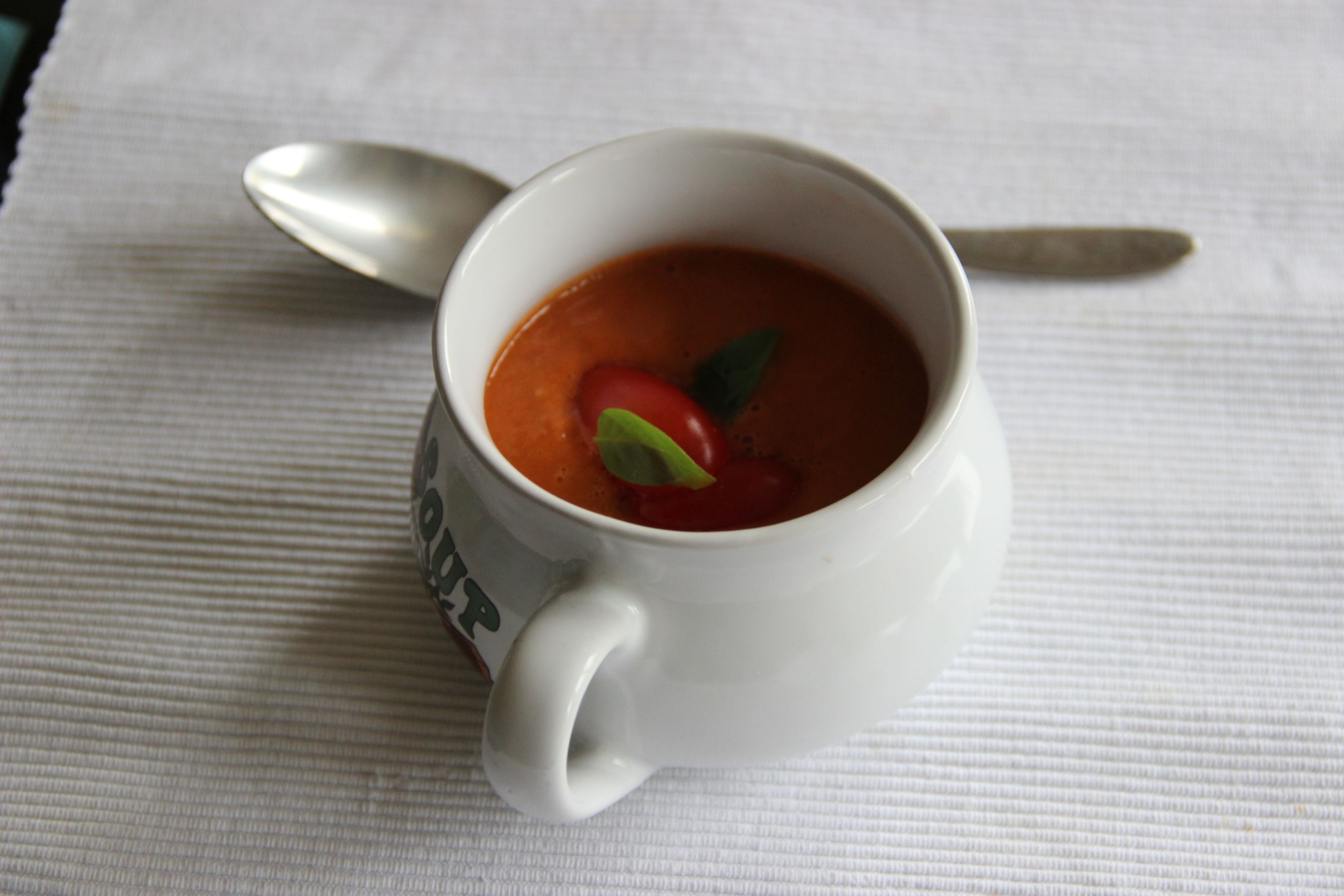 Delicious creamy tomato soup served in a white cup with basil garnish and spoon.