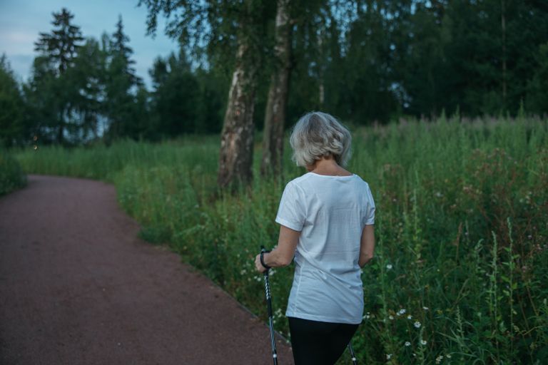 Elderly woman practicing Nordic walking on a park trail, promoting health and fitness.