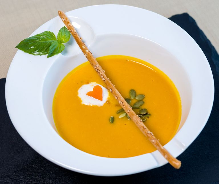 Elegant pumpkin soup garnished with cream and a sesame breadstick, perfect for fine dining visuals.