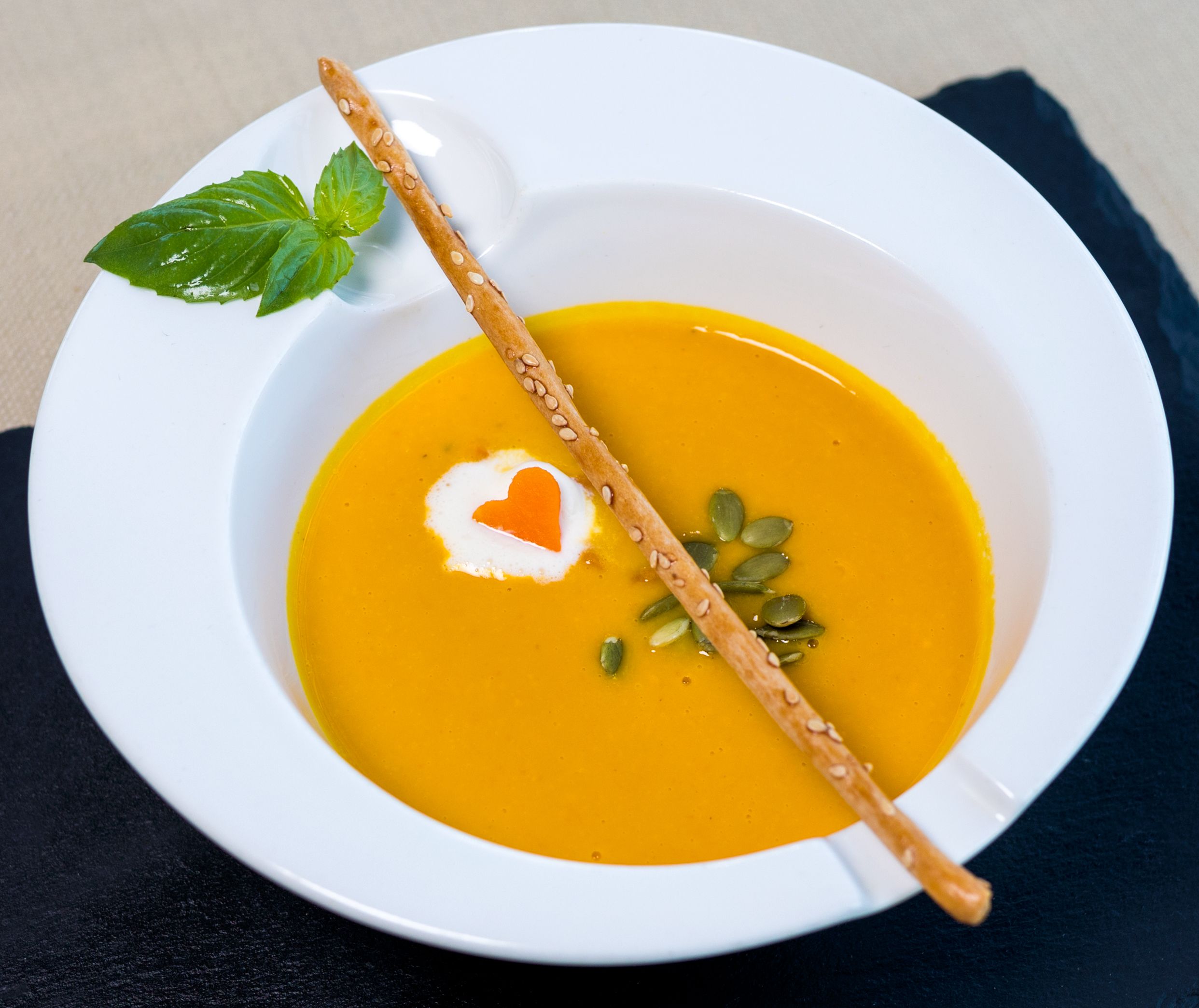 Elegant pumpkin soup garnished with cream and a sesame breadstick, perfect for fine dining visuals.