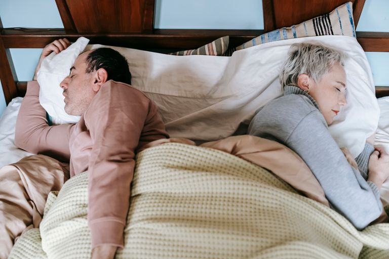 From above side view of middle aged diverse spouses in warm clothes sleeping lying back to back in comfortable bed in morning