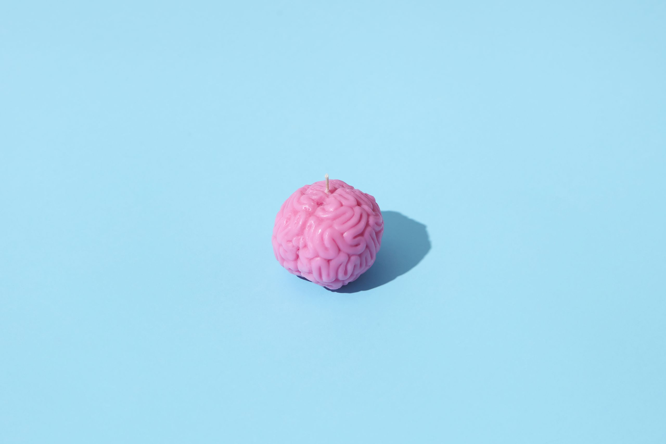 Pink brain-shaped candle on a light blue background, casting a shadow.