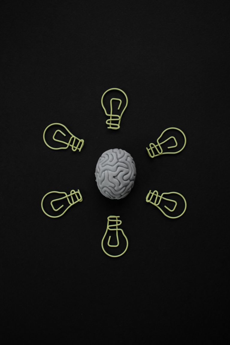 Top view of a brain model surrounded by paper clip light bulbs on black background.