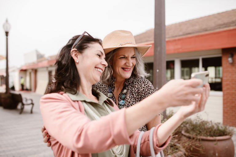 Two smiling women capturing a joyful selfie outdoors on a sunny day.