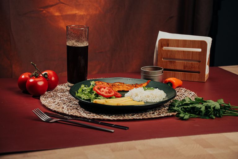 A beautifully arranged plate of rice, grilled chicken, and vegetables set on a dining table.