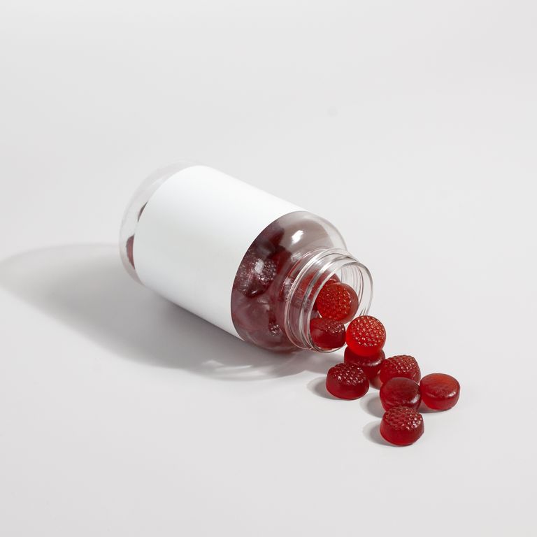 A bottle of red gummy vitamins spills onto a white surface, showcasing product details.