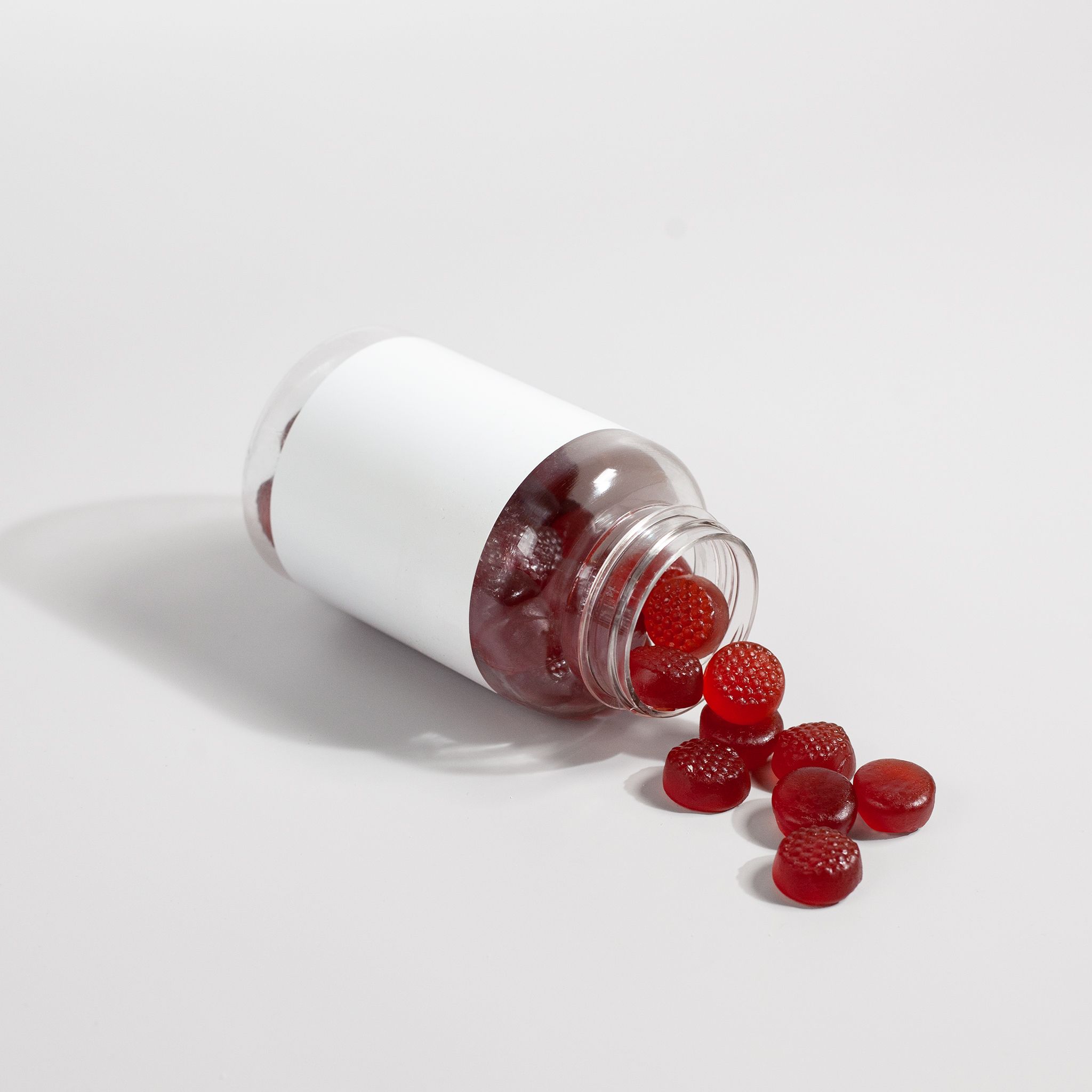A bottle of red gummy vitamins spills onto a white surface, showcasing product details.