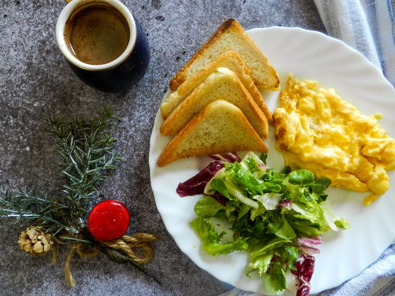 A breakfast plate with scrambled eggs, toast, salad, and coffee on a marble surface.