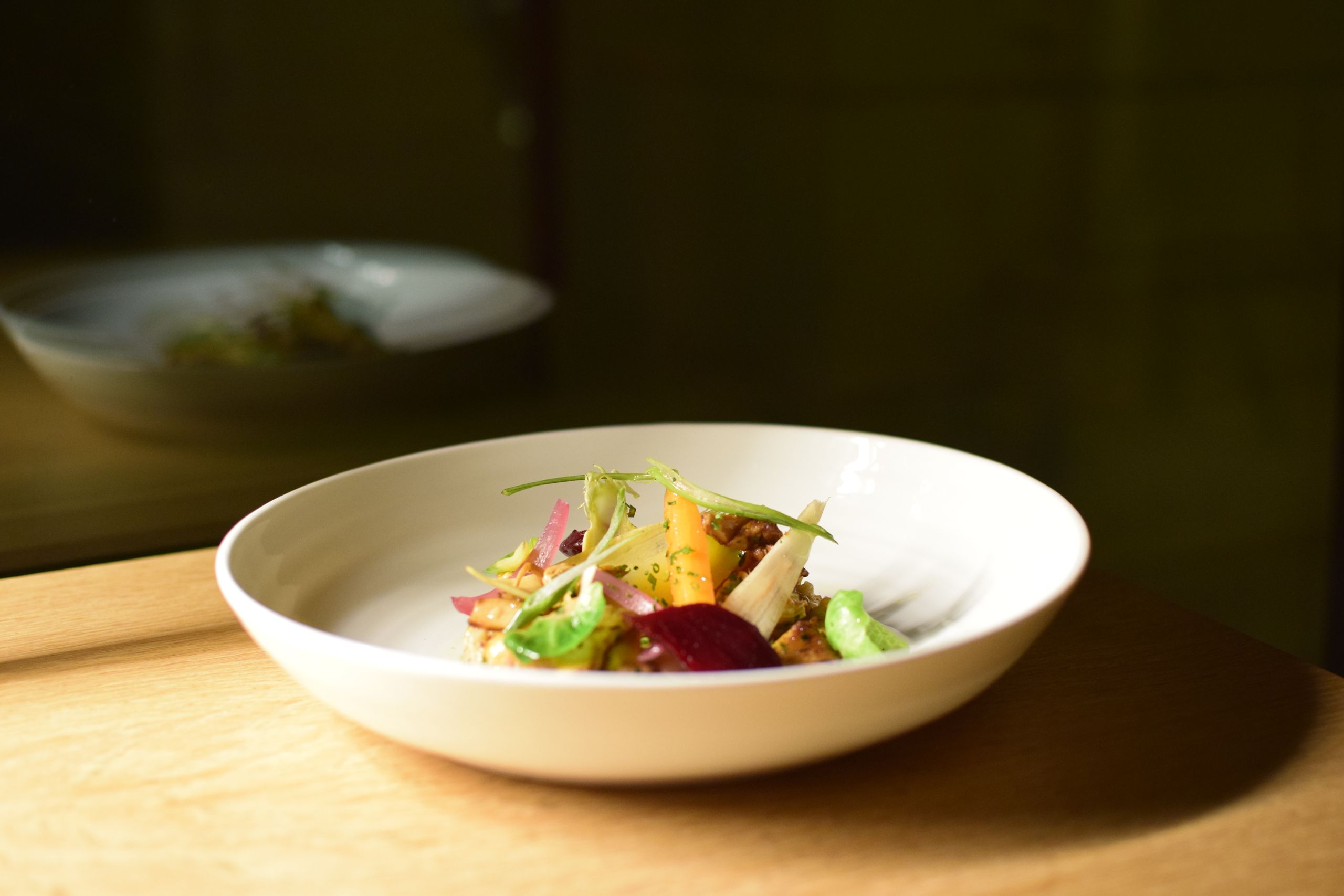 A carefully plated gourmet salad highlighted by natural light on a wooden table.