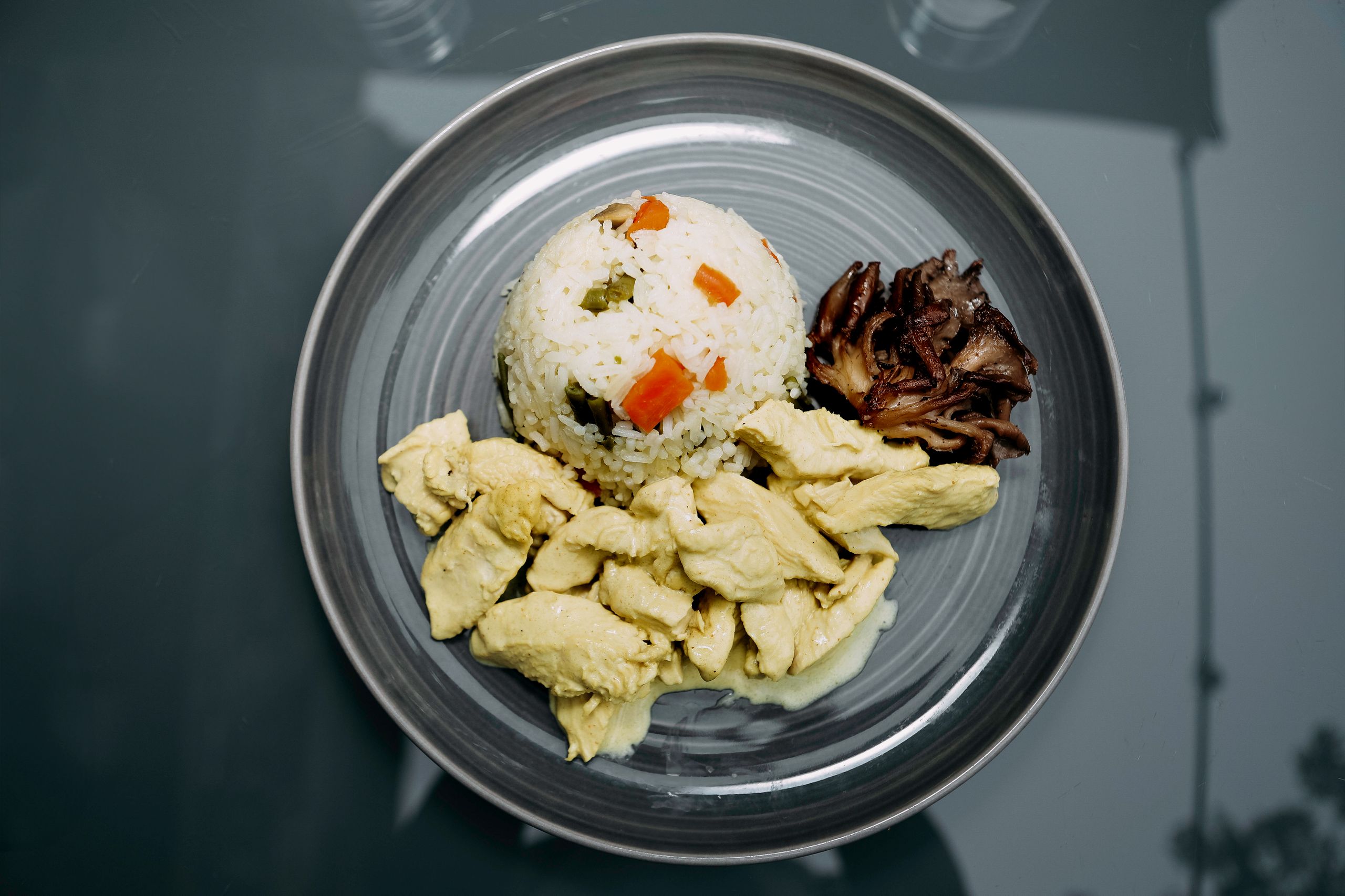 A carefully plated meal featuring chicken, vegetable rice, and mushrooms on a ceramic plate.