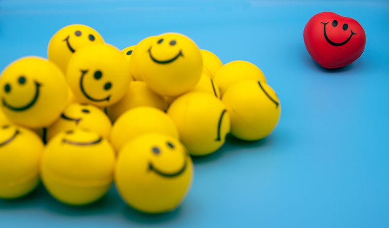 A collection of yellow smiley balls with a red heart-shaped smiley on a blue background.