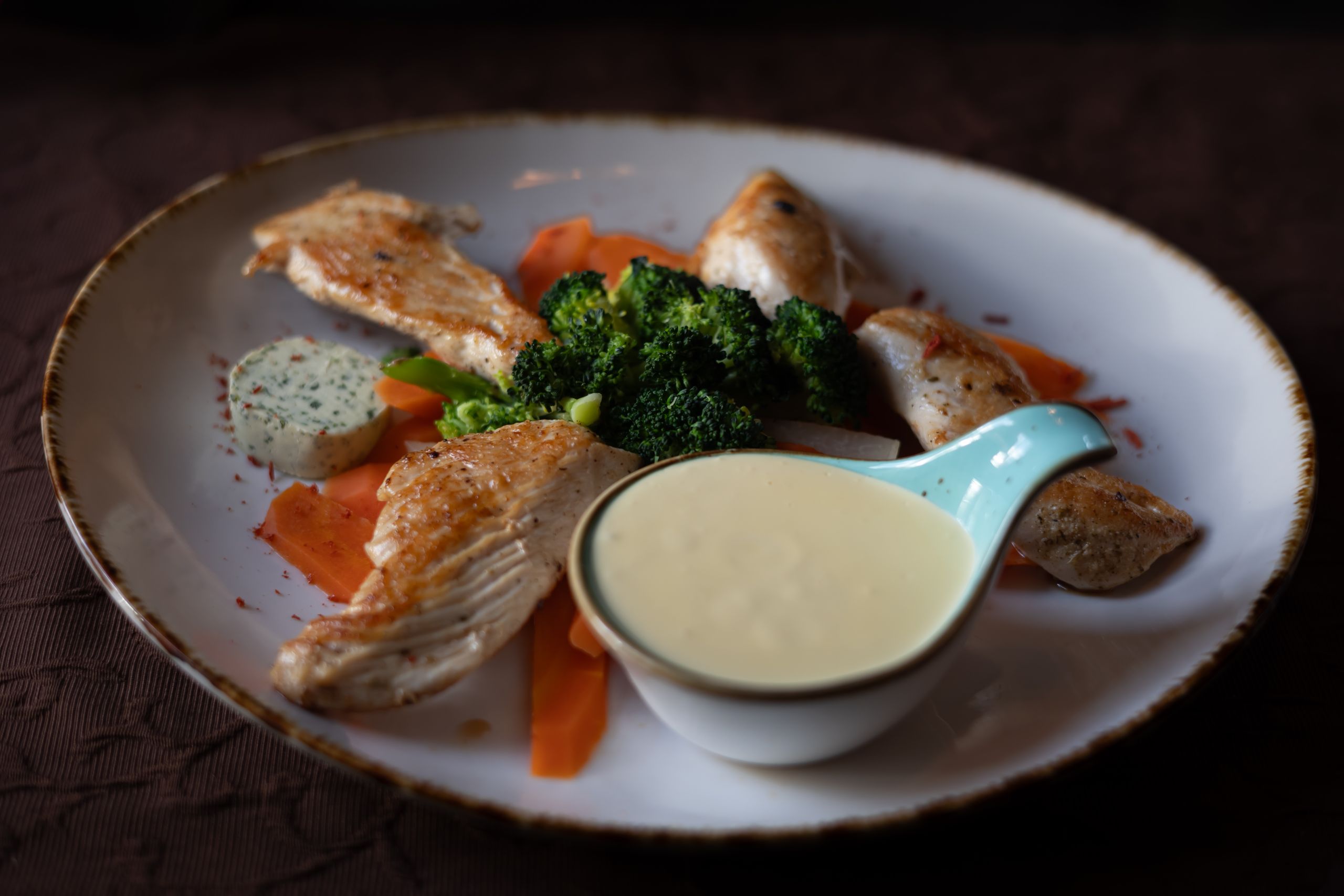 A delectable plate of grilled chicken breast with broccoli, carrots, and a side of creamy sauce.