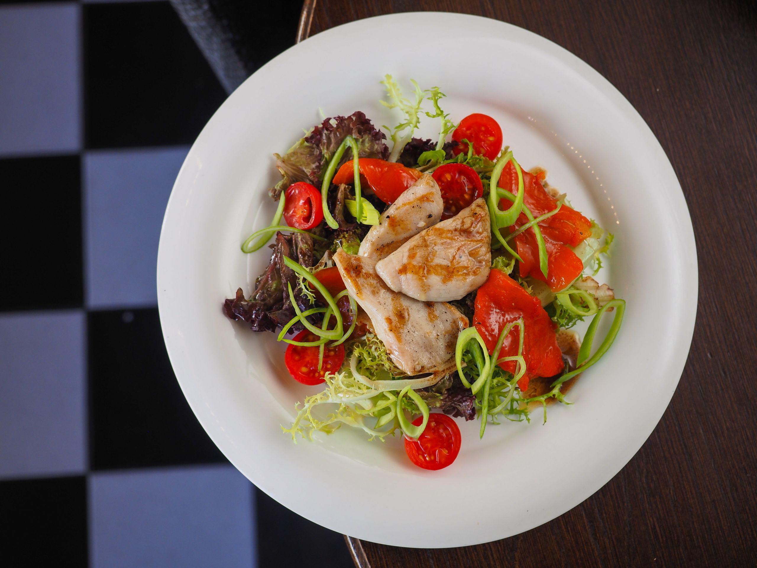 A delicious grilled chicken salad with vibrant vegetables on a white plate.