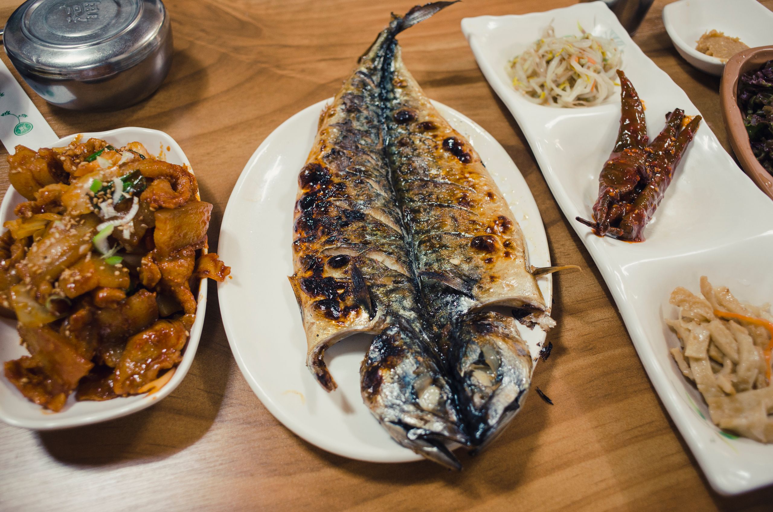 A delicious Korean dinner featuring grilled saba fish, side dishes, and a wooden table setting.