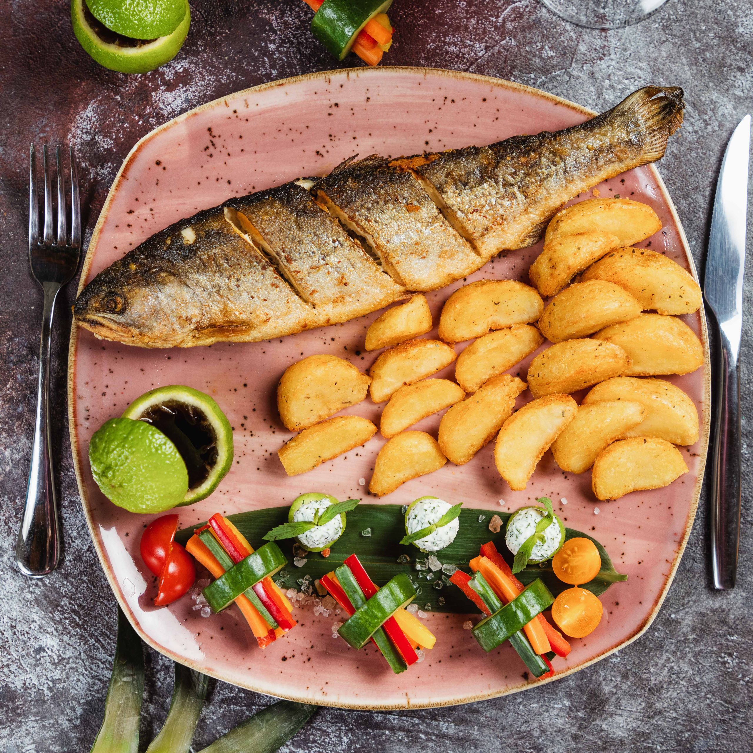 A delicious plate of grilled fish with crispy potato wedges and colorful vegetables.