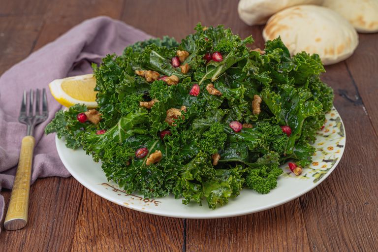 A fresh kale salad topped with walnuts and pomegranate seeds, served with lemon.