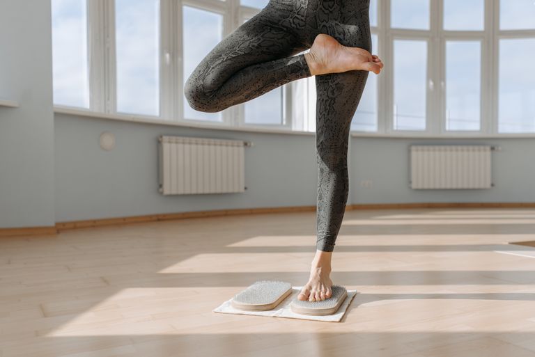 A person practicing yoga balance on wooden floor in a bright room.