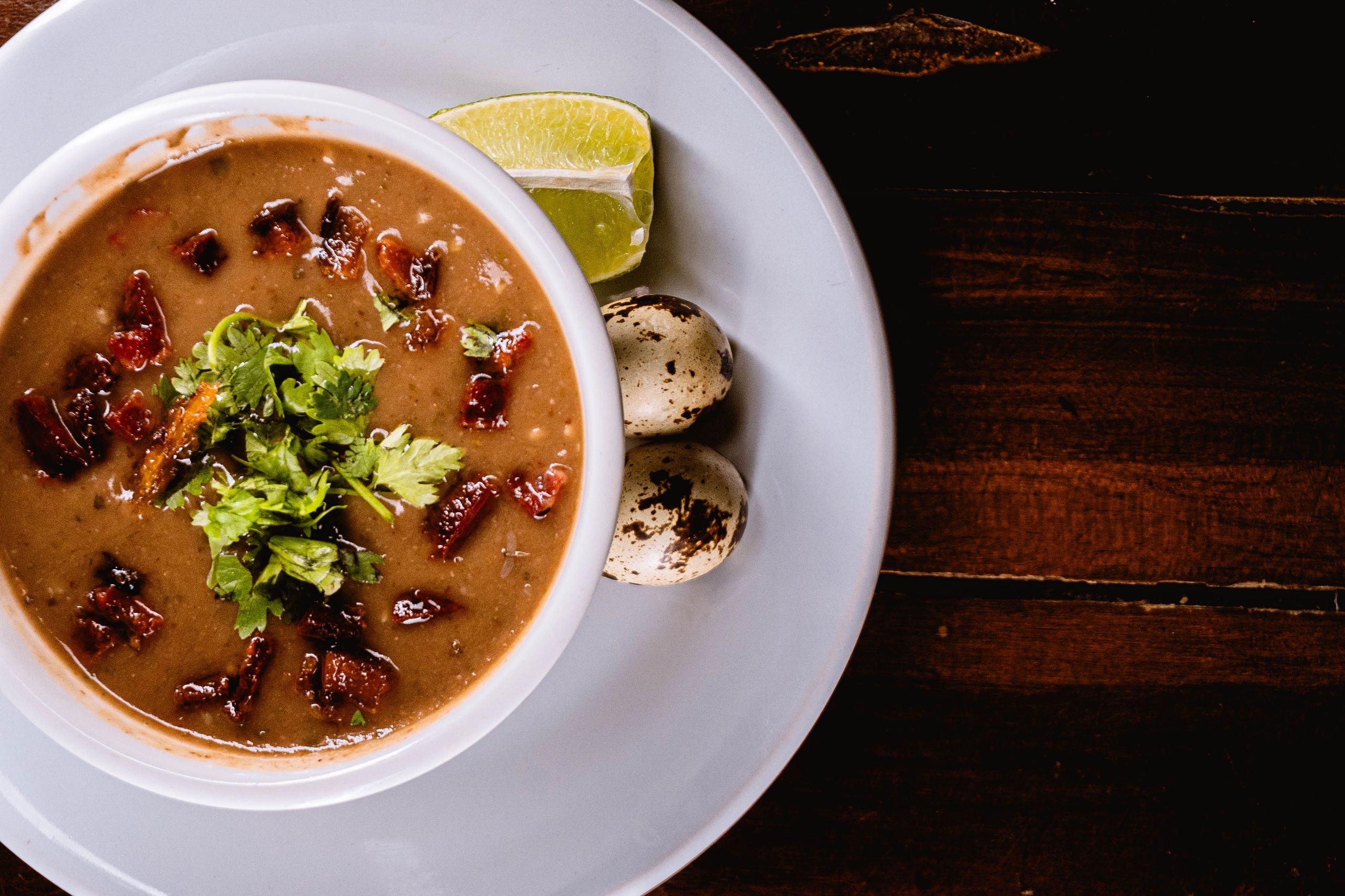 A savory bean soup garnished with herbs, quail eggs, and lime, perfect for a hearty meal.