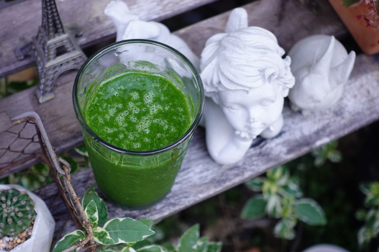 A vibrant green smoothie next to angel statue and Eiffel Tower model outdoors.