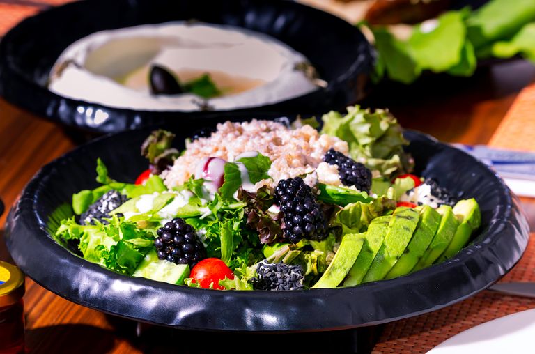 A vibrant mixed salad with blackberries, avocado, lettuce, and grains in a black bowl.