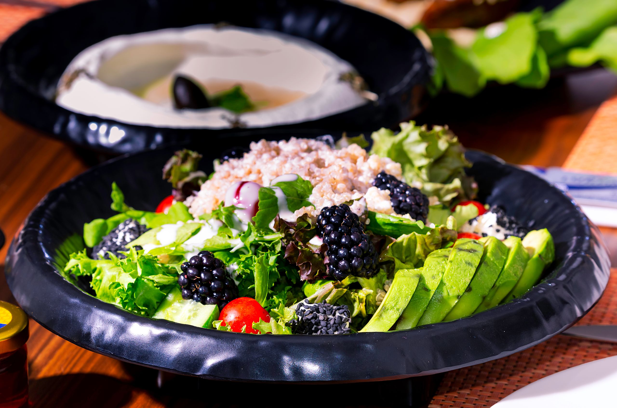 A vibrant mixed salad with blackberries, avocado, lettuce, and grains in a black bowl.