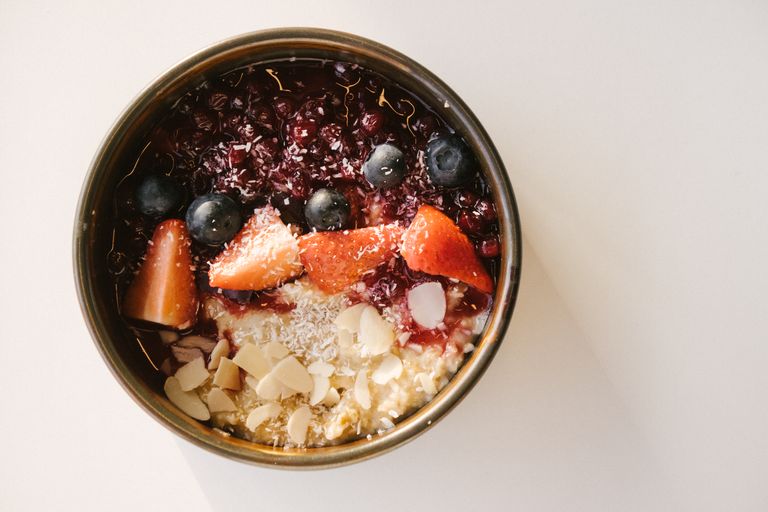 A vibrant oatmeal breakfast bowl with berries and almonds on a white surface.