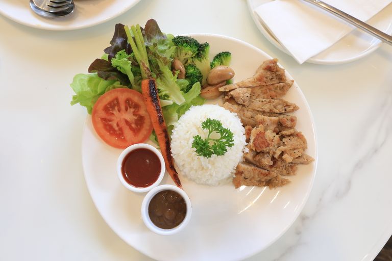 A vibrant plate of grilled chicken, rice, fresh vegetables, and sauces. Perfect for food lovers.
