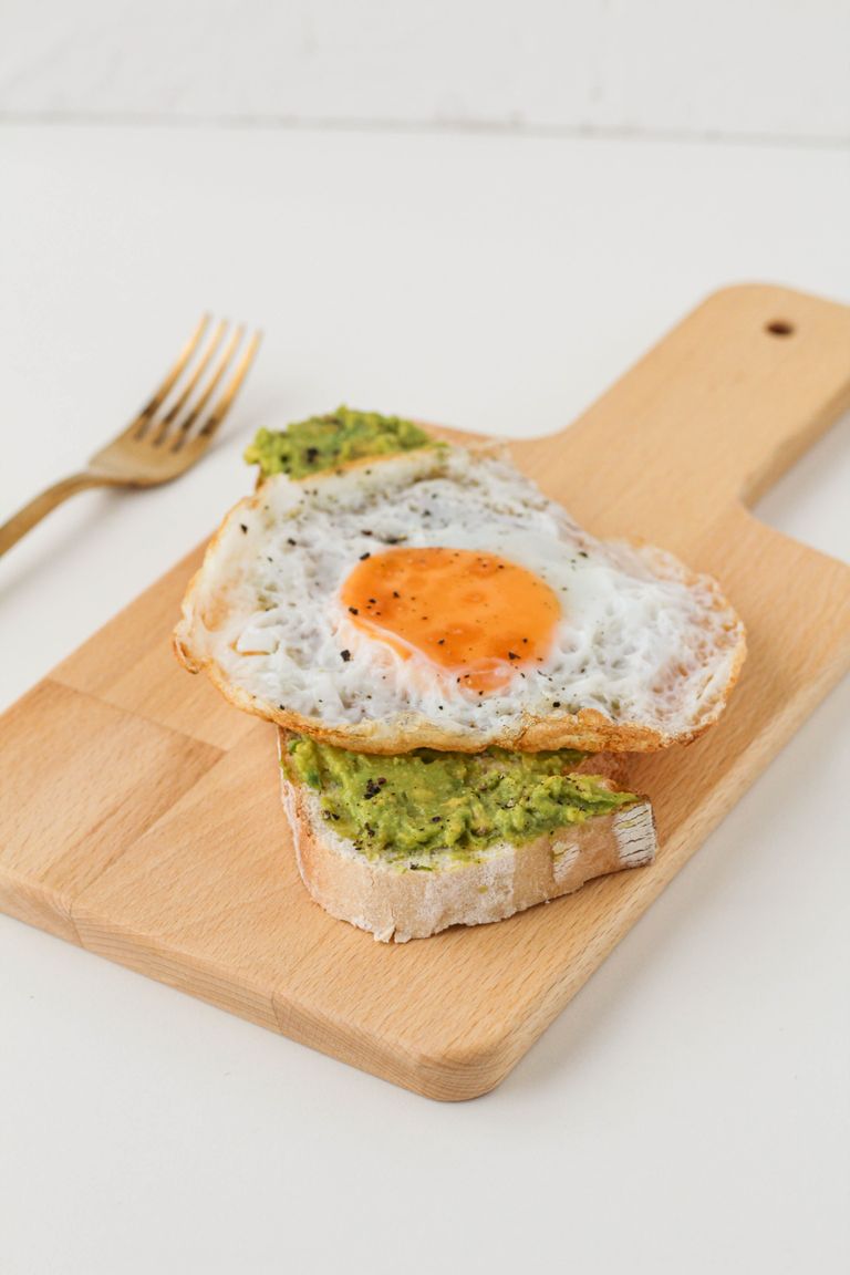 Appetizing avocado toast topped with a fried egg on a wooden board.