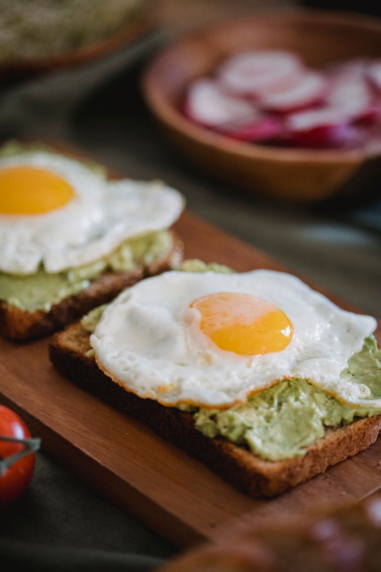 Appetizing avocado toast topped with sunny-side-up eggs on a wooden board.