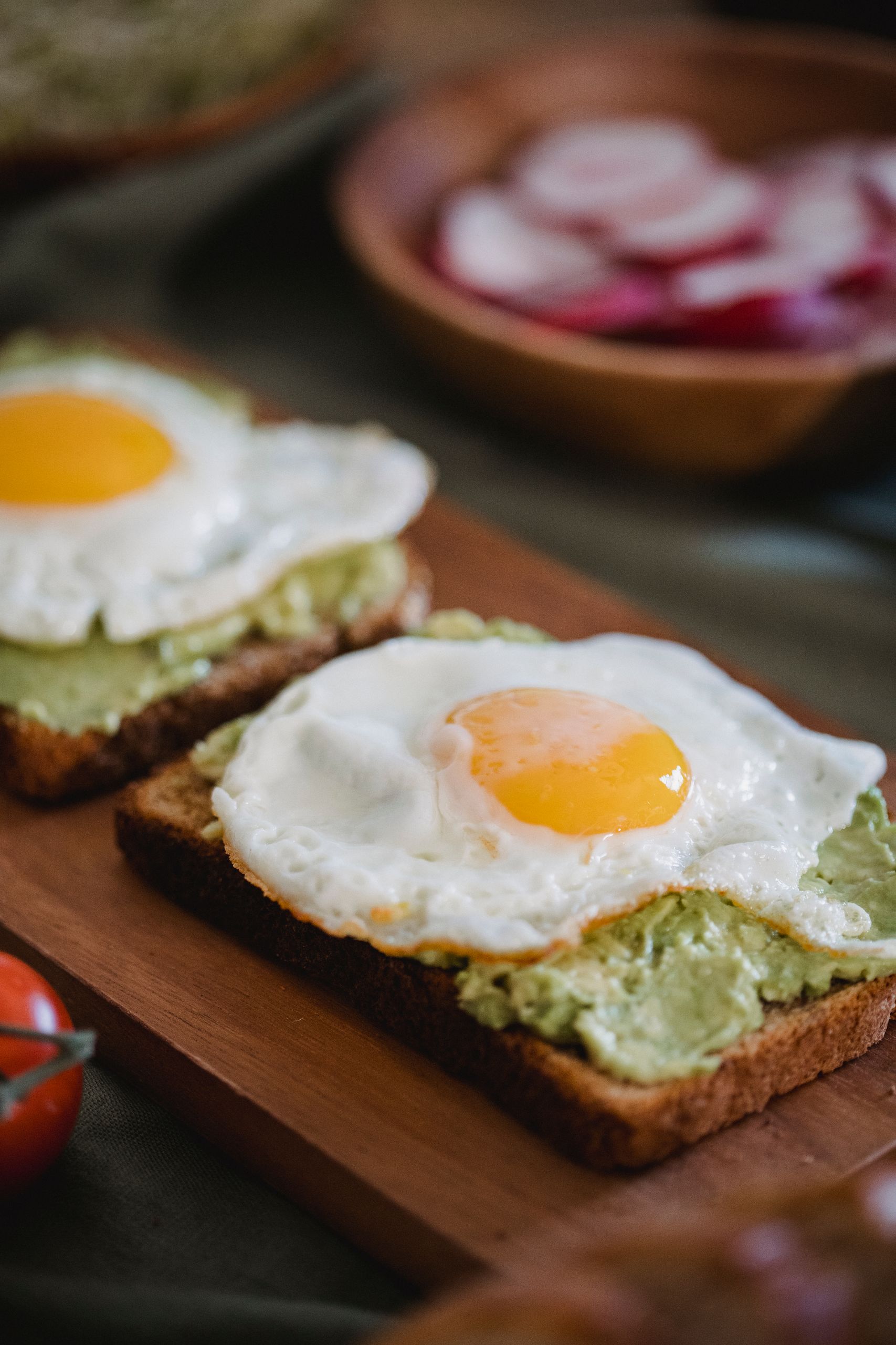 Appetizing avocado toast topped with sunny-side-up eggs on a wooden board.