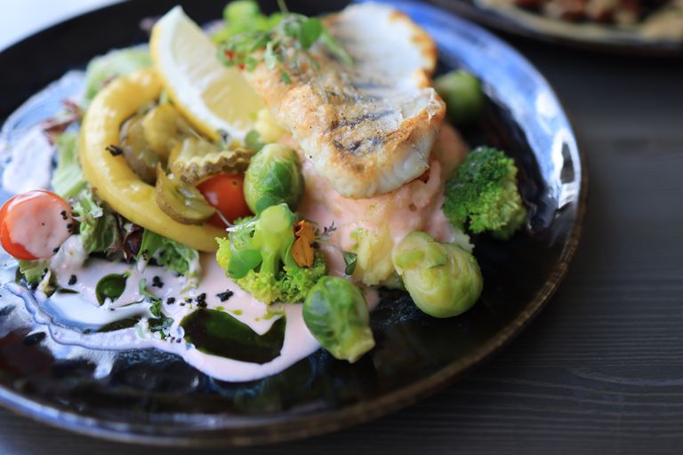 Close-up of a gourmet fish dish with assorted vegetables on a dark plate.