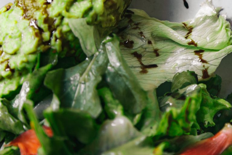 Close-up of a vibrant salad with lettuce and avocado spread, drizzled with balsamic dressing.