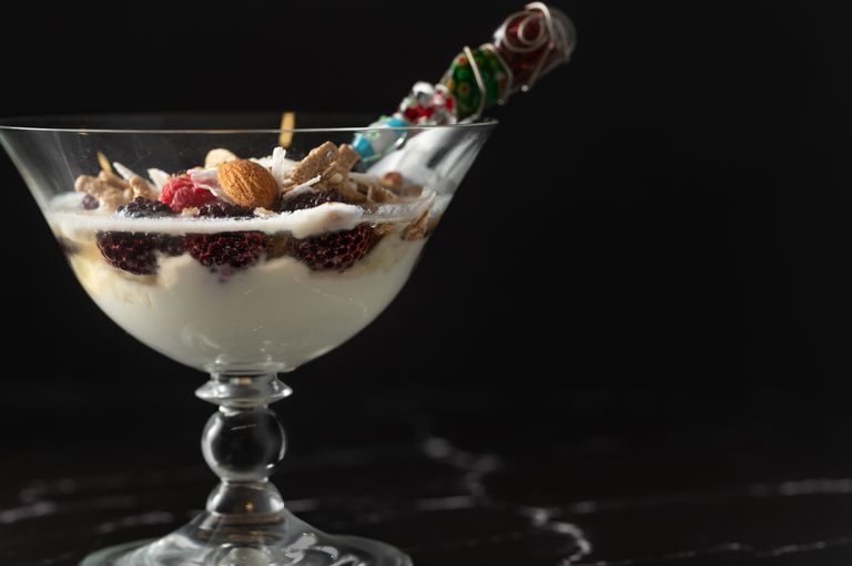 Close-up of a yogurt dessert with berries and nuts in a decorative glass on a dark background.
