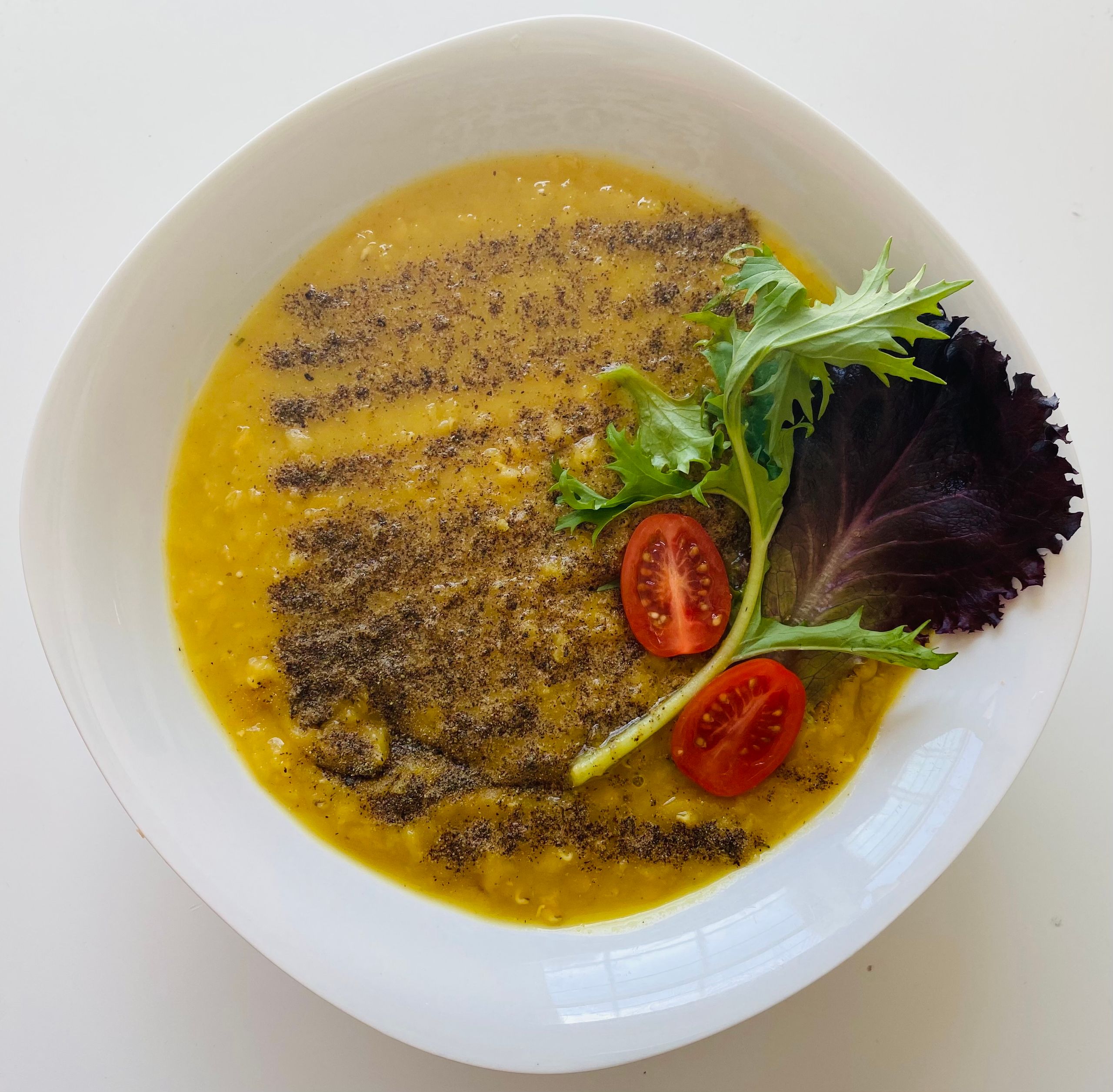 Close-up of creamy lentil soup garnished with greens and tomatoes in a white bowl.