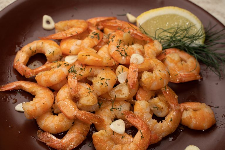 Close-up of flavorful shrimp garnished with garlic, lemon, and dill.