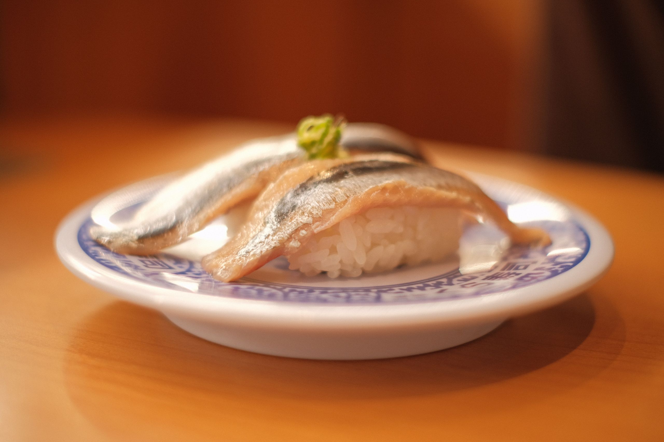 Close-up of fresh horse mackerel sushi served on a decorative porcelain plate with rice.