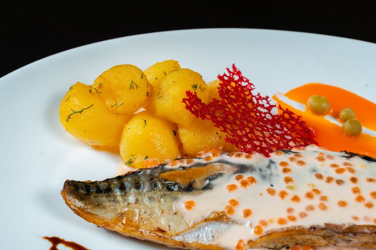 Close-up of gourmet fish dish with creamy sauce, potatoes, and red garnish.