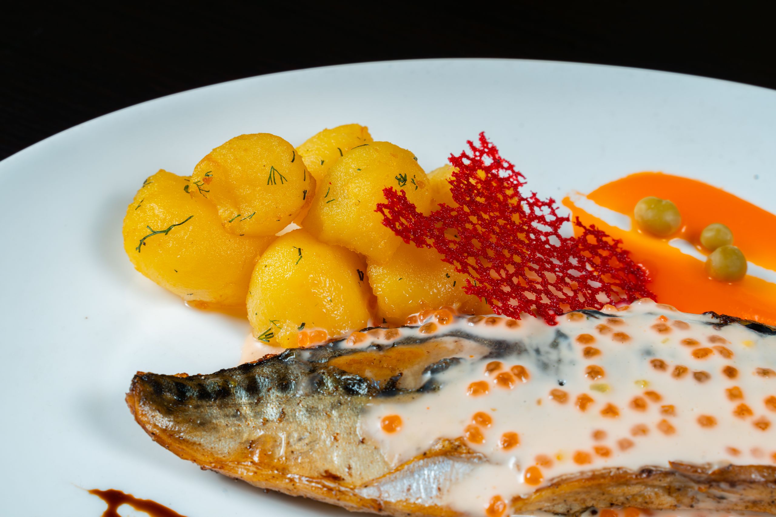 Close-up of gourmet fish dish with creamy sauce, potatoes, and red garnish.