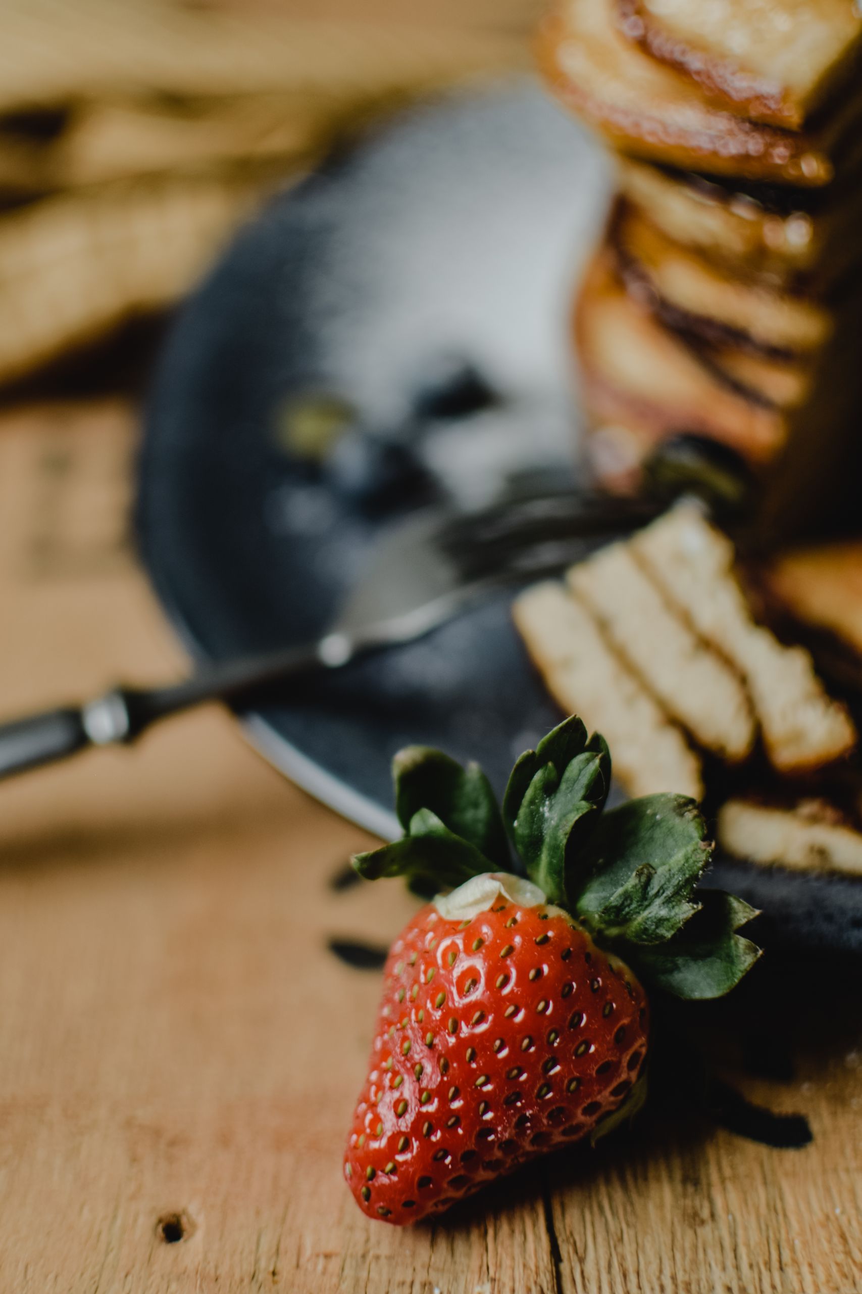 Close-up of layered pancakes with fresh strawberries on a wooden table.