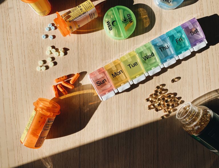 Colorful pill organizer with medication bottles and tablets on a wooden surface.