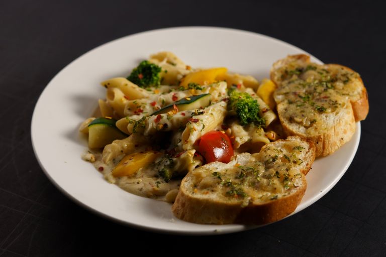 Creamy pasta loaded with vegetables paired with flavorful garlic bread on a plate.