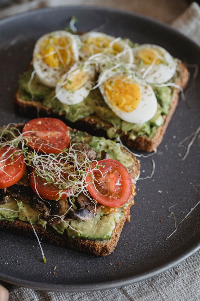 Delicious avocado toast topped with sliced eggs, tomatoes, and sprouts, perfect for a nutritious meal.