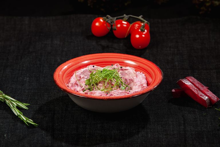Delicious beetroot salad with chives served in a vibrant red ceramic bowl on a dark background.